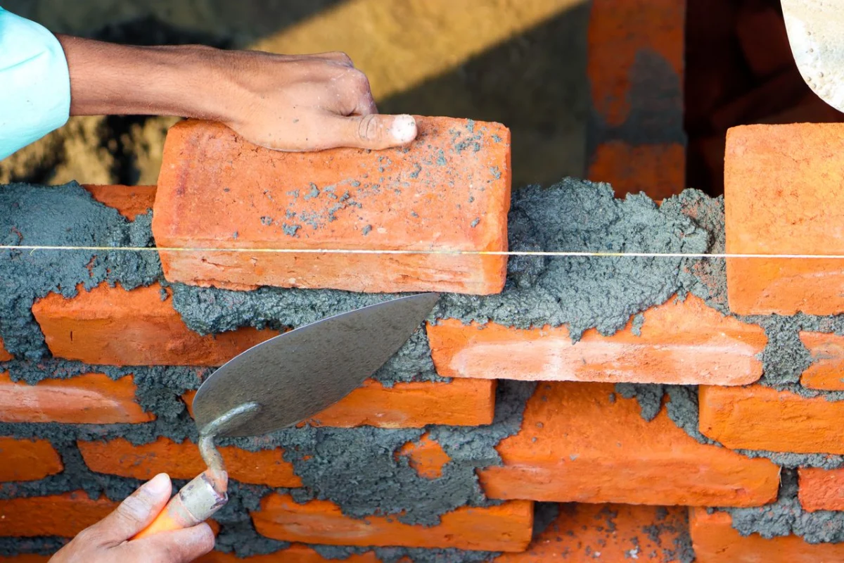Hands laying bricks with mortar and a trowel