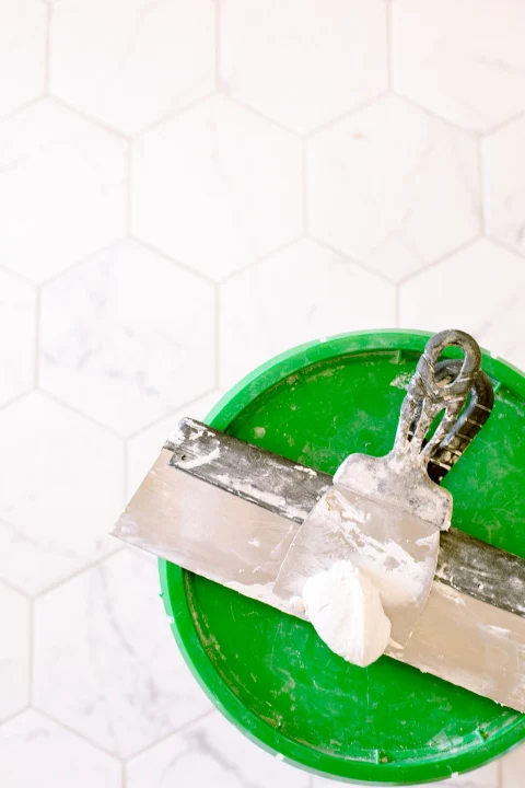 Grout float and bucket on a white hexagon tile floor