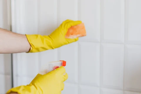 Gloved hands cleaning white wall tile