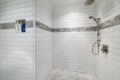 White tiled shower with a niche and a mosaic accent band